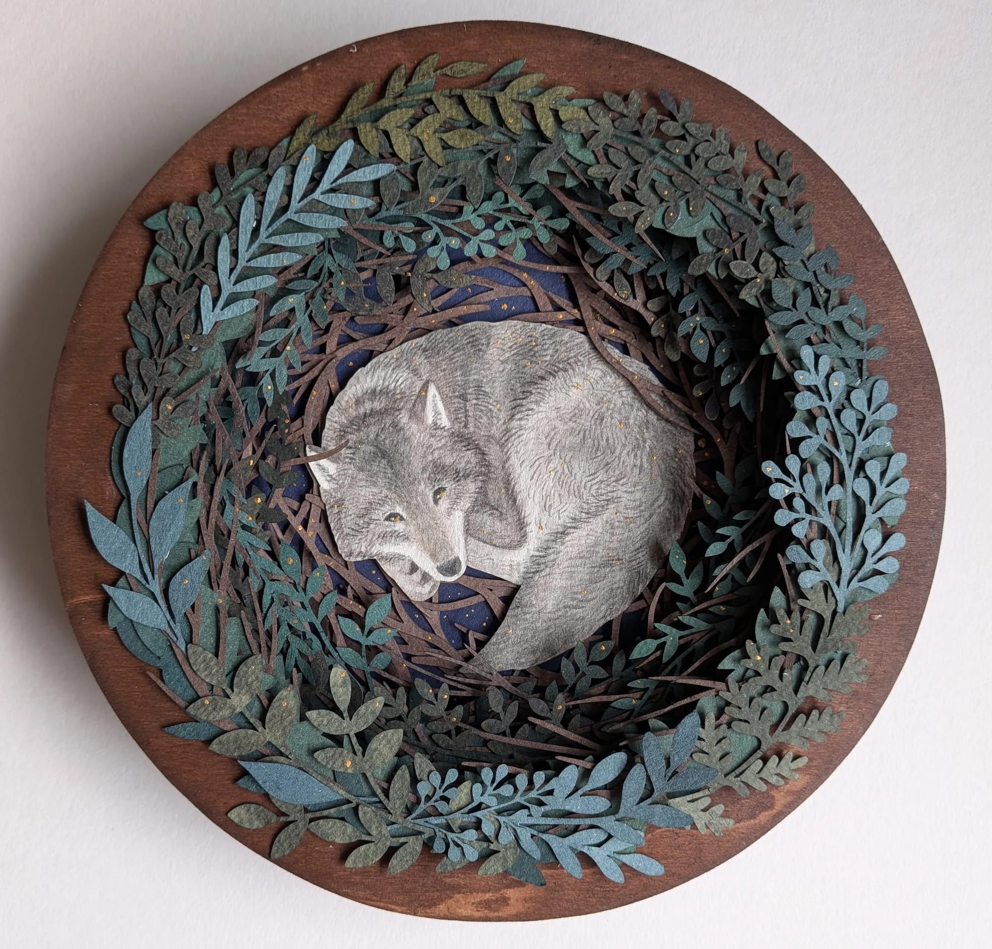 A paper collage with a sleeping wolf surrounded by foliage